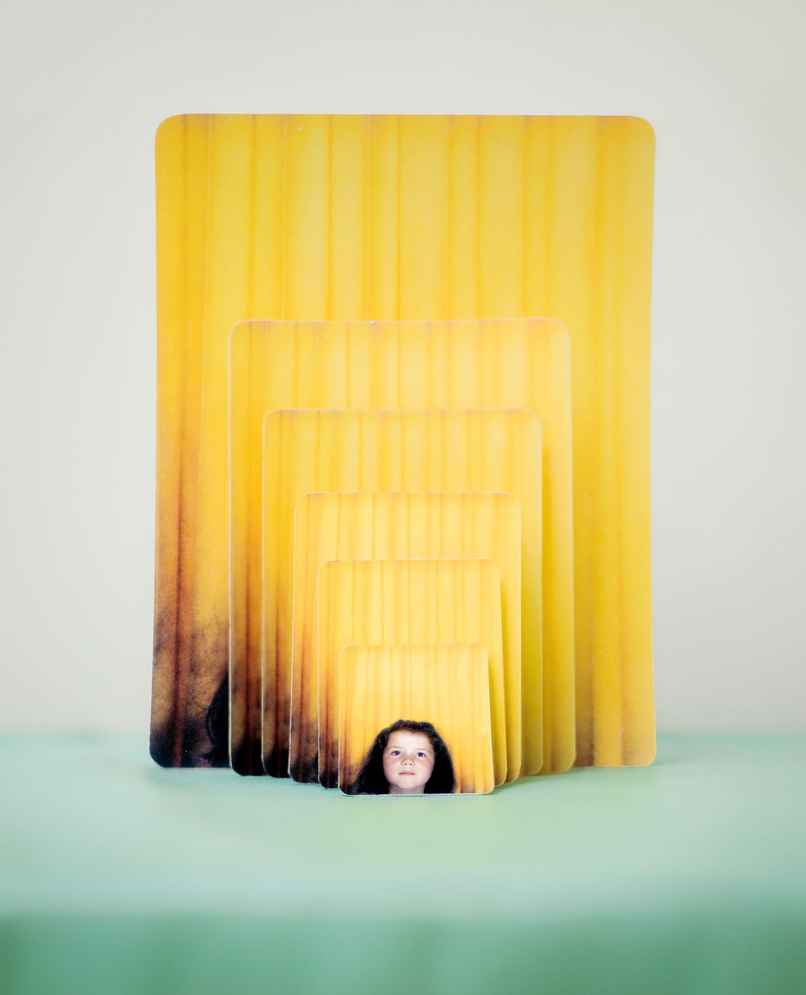 The same photo of a girl in front of a yellow curtain, printed in different sizes and displayed in a cascade.
