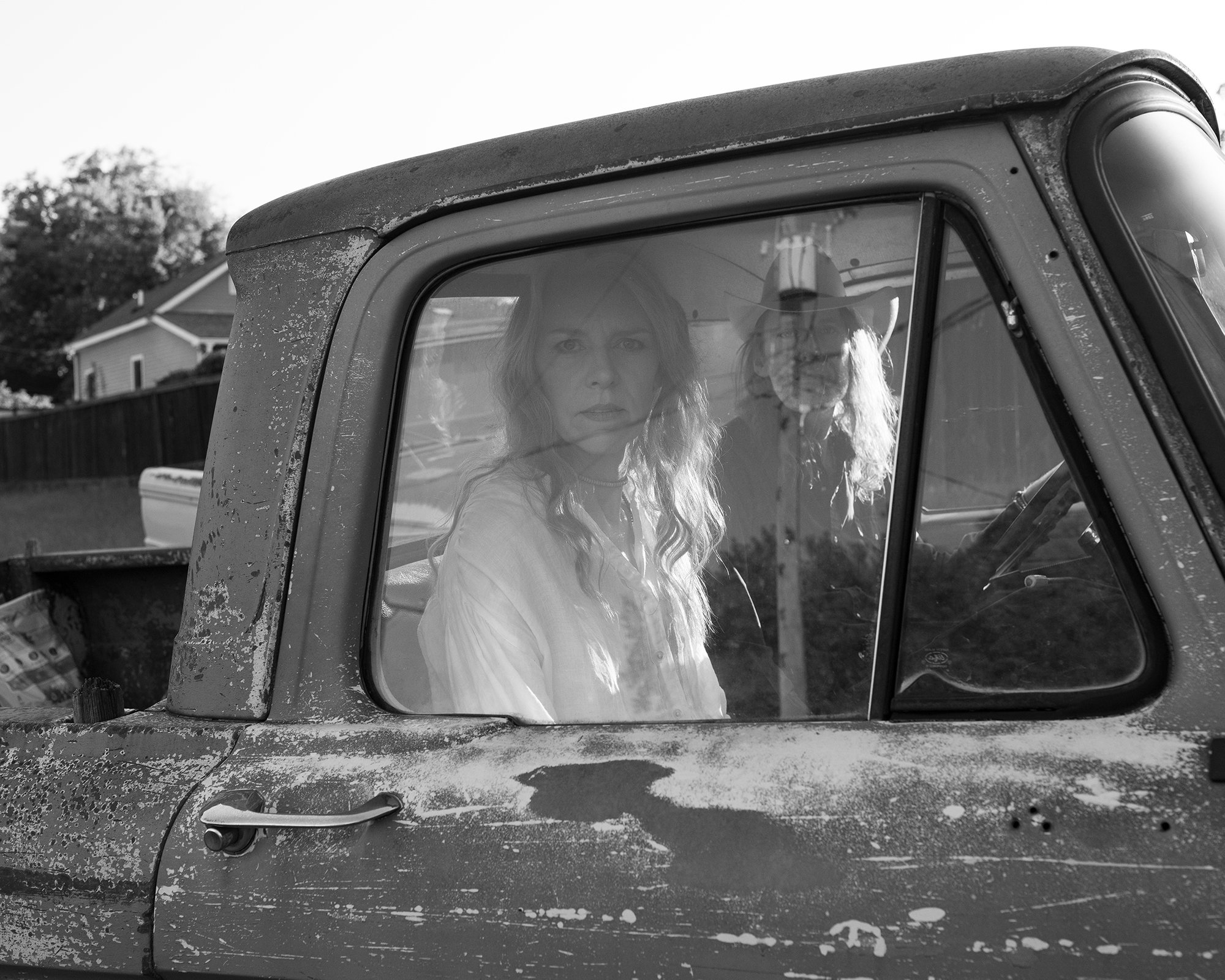 Two people looking sternly out of the side window of an old worn pickup truck.